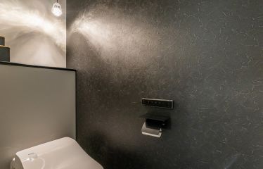 ブラックのアクセントクロスにお施主様支給の照明がマッチした、ホテルライクなトイレ。