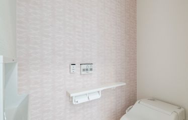 ペールピンクのリボン柄アクセントクロスが可愛らしさを引き立てるトイレ。タンクレストイレ、独立型手洗い器を採用してすっきりと。