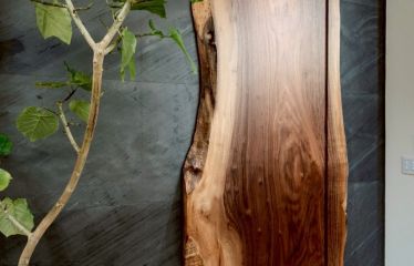 一枚板の天然木で作られたこだわりの扉。木の形を活かしたデザインが、ブラックの天然石材と見事に調和。リビングで洗練された存在感を放っています。