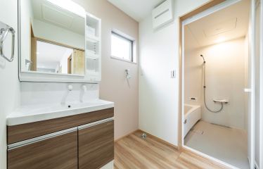やさしいピーチピンクのアクセントクロスが彩る洗面空間。水回りをまとめて、家事動線もすっきり。