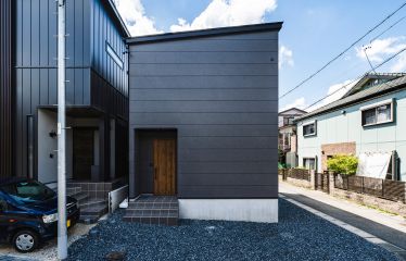 ダークグレーのシックな外壁に、温かみのあるマキアートパインのドアがアクセント。 正面は窓を設けずプライバシーにも配慮したファサードデザインです。