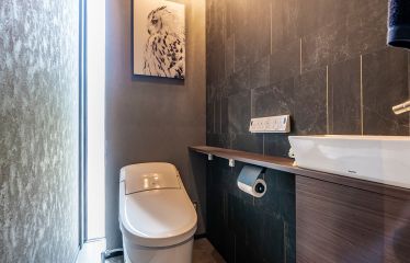 ご主人好みの暗めでシックなトイレに、こだわりの絵とライトが映えています。 背後の隠し収納ですっきりと整った空間に。