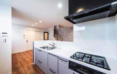 くすみ感のあるグレイッシュベージュのキッチンが、空間をやさしく整えます。照明はダウンライトを縦に美しく配置し、すっきりとした印象に。