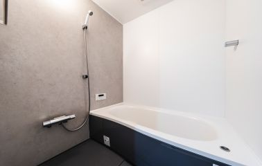 モルタル調の壁が存在感を放つマテリアルなバスルーム。ミディアムグレーの足元が上質な落ち着きを添えています。