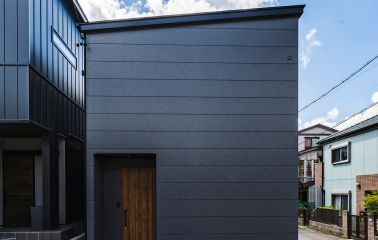 ダークグレーのシックな外壁に、温かみのあるマキアートパインのドアがアクセント。 正面は窓を設けずプライバシーにも配慮したファサードデザインです。